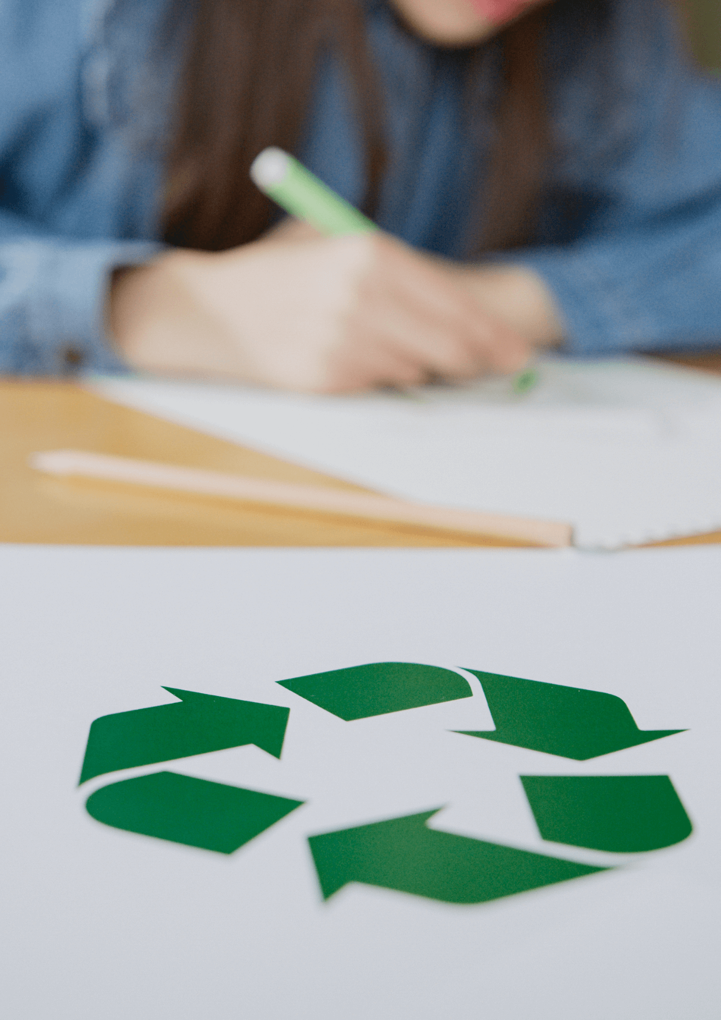 kobieta przy biurku rysuje zielone logo recyklingu