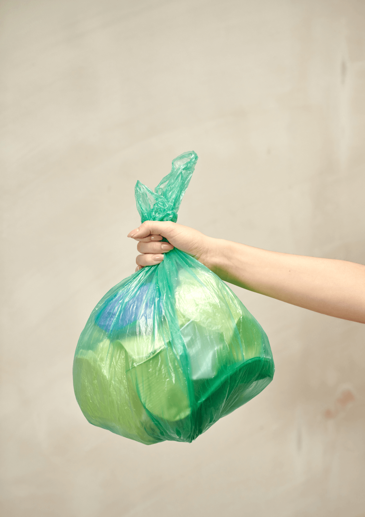 ręka trzyma wypełniony zielony worek na odpady